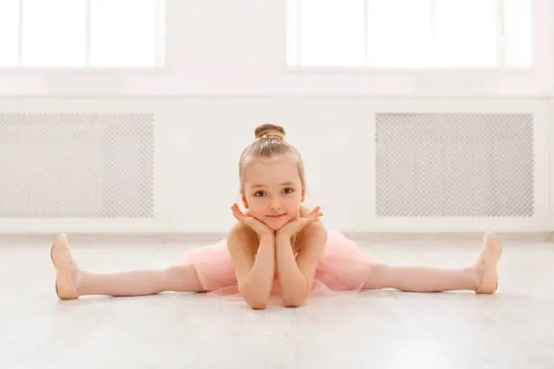 Little ballerina in split on floor, copy space. Smiling baby girl dreaming to become professional ballet dancer, classical dance school