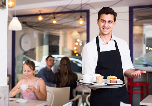 Smiling waiter is warmly welcoming guests to cozy coffeehouse.