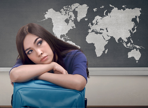 Tired asian traveler woman lying down on a suitcase against world map on blackboard
