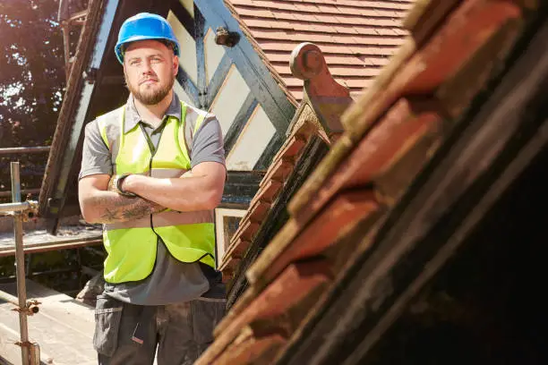 a builder or roofer is posing to camera on the roof of a renovation project