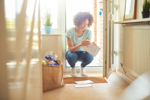 coming home to bills a woman returns home from the shops and finds some letters on the mat . She bends down to open them . key doormat stock pictures, royalty-free photos & images