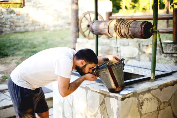 Young man drinking water from draw well