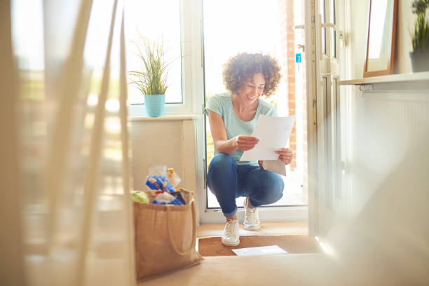 good news on the doorstep a woman returns home from the shops and finds some letters on the mat . She bends down to open them and smiles at what she is reading key doormat stock pictures, royalty-free photos & images