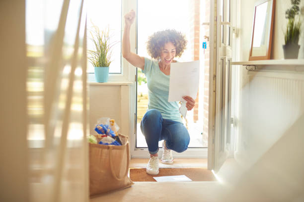 got the job a woman returns home from the shops and finds some letters on the mat . She bends down to open them and smiles at what she is reading and punches the air in celebration key doormat stock pictures, royalty-free photos & images