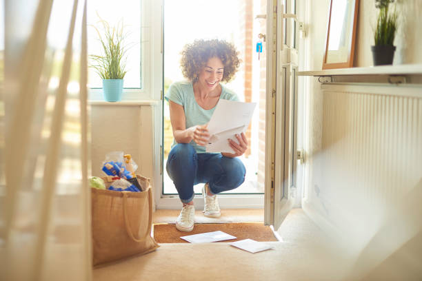 happy letter a woman returns home from the shops and finds some letters on the mat . She bends down to open them and smiles at what she is reading key doormat stock pictures, royalty-free photos & images