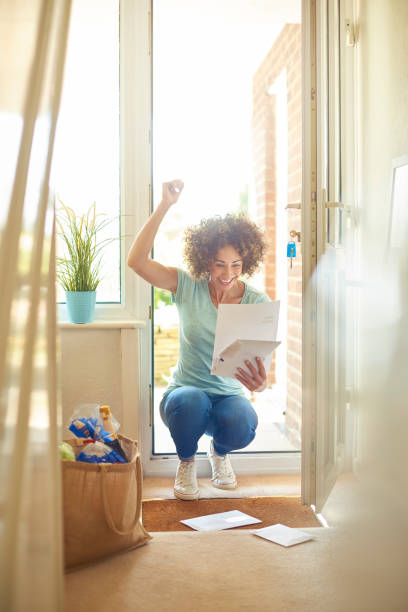 she got the job a woman returns home from the shops and finds some letters on the mat . She bends down to open them and smiles at what she is reading and punches the air in celebration key doormat stock pictures, royalty-free photos & images