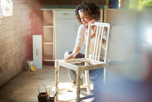 a woman restores and improves an old wooden chair in her workshop