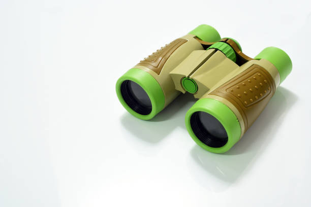 Little boy  is using binoculars in front of orange colored background with a cute smile