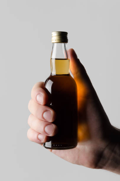miniaturowe duchy / alkohol butelka mock-up - męskie ręce trzymając butelkę alkoholu na szarym tle - whisky scotch whisky schnapps liqueur brandy zdjęcia i obrazy z banku zdjęć