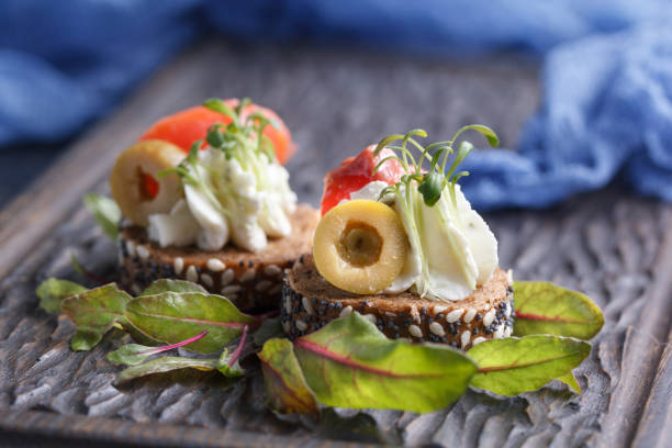 istock Delicious canape with salmon, cottage cheese, olive with micro greens on a dark background. Cold appetizer. 813754084