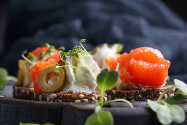 istock Delicious canape with salmon, cottage cheese, olive with micro greens on a dark background. Cold appetizer. 813762912