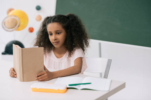istock Concentrated african american schoolgirl reading textbook in class 813774370