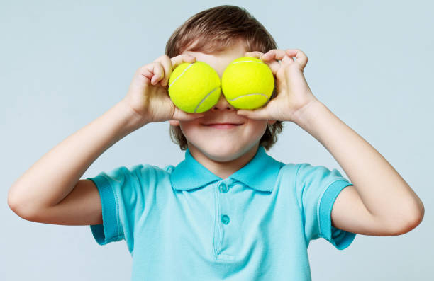 pequeño muchacho con pelotas de tenis en lugar de los ojos, sonriendo - tennis child childhood sport fotografías e imágenes de stock