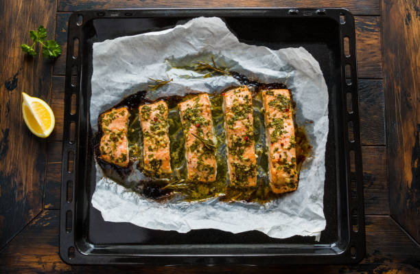 lachs im ofen mit butter, petersilie und knoblauch gebraten. gekochten fisch auf ein backblech auf den hölzernen hintergrund, ansicht von oben. - pink peppercorn pepper pink herb stock-fotos und bilder