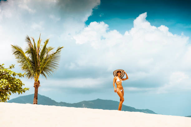 Woman at tropical beach in long dress and sun hat
