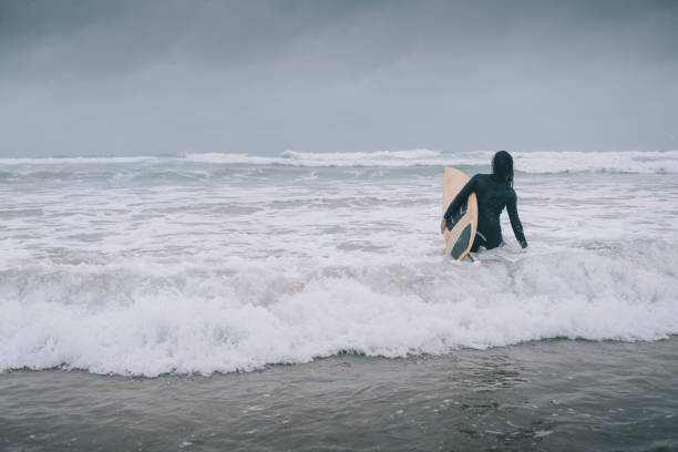 istock Female Surfer wading into the sea with Surfboard. 813865466