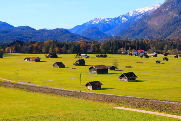 sopra le fattorie e gli chalet del fienile, il villaggio alpino di sunny garmisch partenkirchen nelle alpi bavaresi dalle alpi, l'idilliaco paesaggio autunnale dei boschi di pini, la maestosa valle delle alpi, il drammatico panorama della catena montuosa t - waxenstein foto e immagini stock