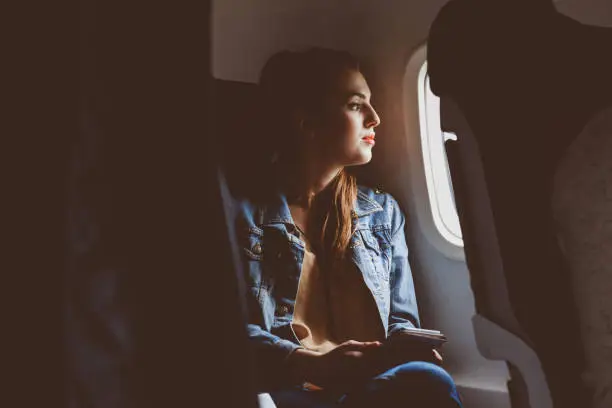 Young female passenger travelling by flight. Female passenger looking outside plane window.