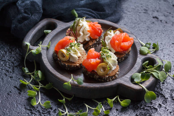 istock Delicious canape with salmon, cottage cheese, olive with micro greens on a dark background. Cold appetizer. 813894980