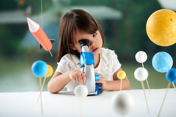 Portrait of Curious Little Scientist Curious little girl looking through microscope while having fun in scientific club for preschoolers, blurred background school science project stock pictures, royalty-free photos & images