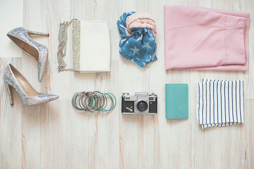 Variety of women's personal accessories organized in knolling arrangement on wooden background. Items include: clothing accessories, shoes, camera, bracelets, purse, scarf, wallet. Mother's Day or fashion themes.