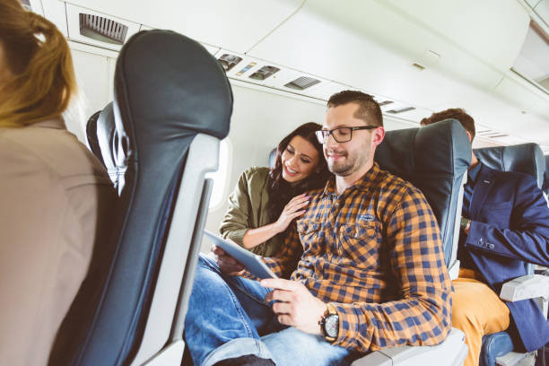 Young people traveling by airplane using digital tablet Happy young people traveling by airplane using digital tablet. Couple flying by plane using tablet pc. economy class stock pictures, royalty-free photos & images