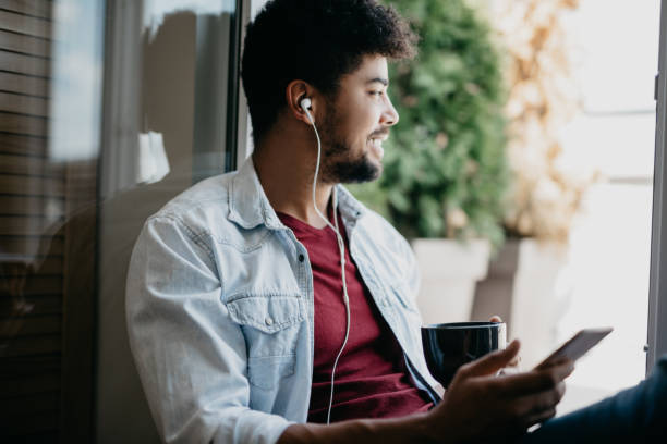 istock Handsome man is looking through the window and listening the podcast 813926694