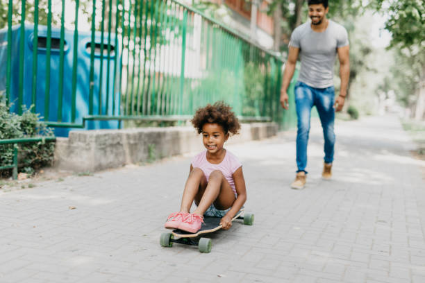 istock Daughter sits on the longboard and gets pushed by her father. 813993192
