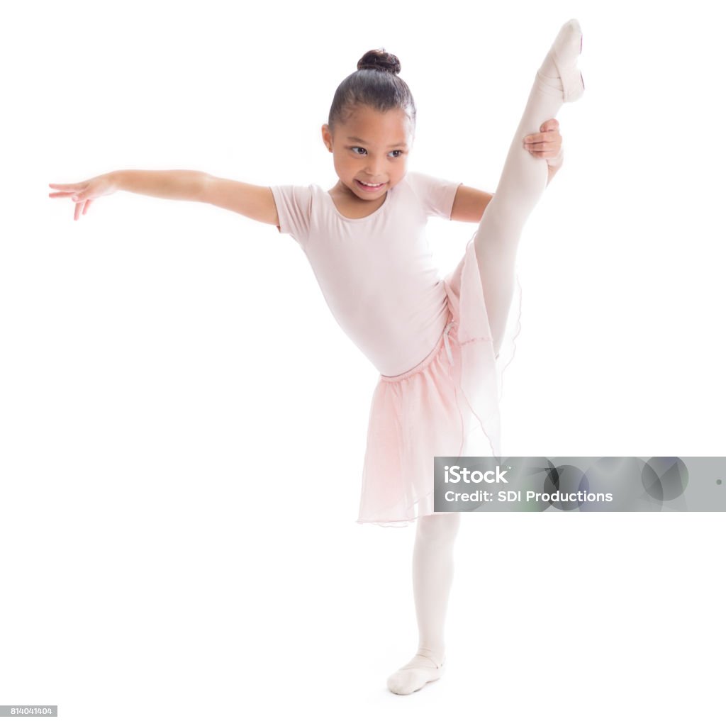 Adorable young African American ballerina in ballet pose Cute preschool age African American female ballerina stretches out her leg in ballet pose. Child Stock Photo