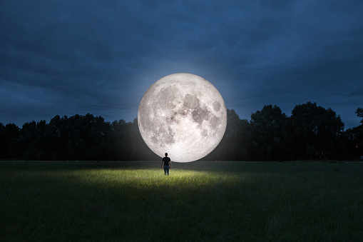 Man standing in front of moon in a park at night. Photomanipulation of man standing in front of moon.