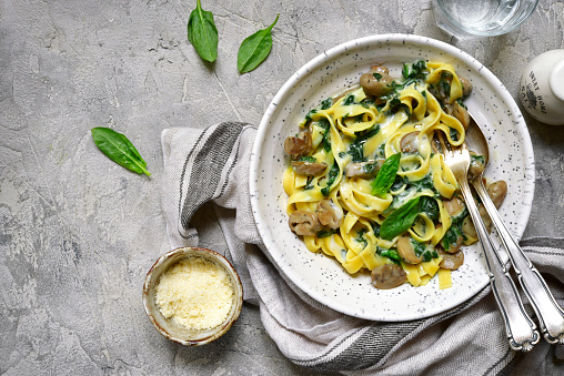 Creamy tagliatelle with mushrooms and spinach in a bowl on a grey slate,stone or concrete background.Top view.