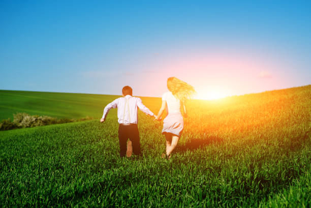 istock Young happy lovers running on meadow with green grass and blue sky, From the back 814082178