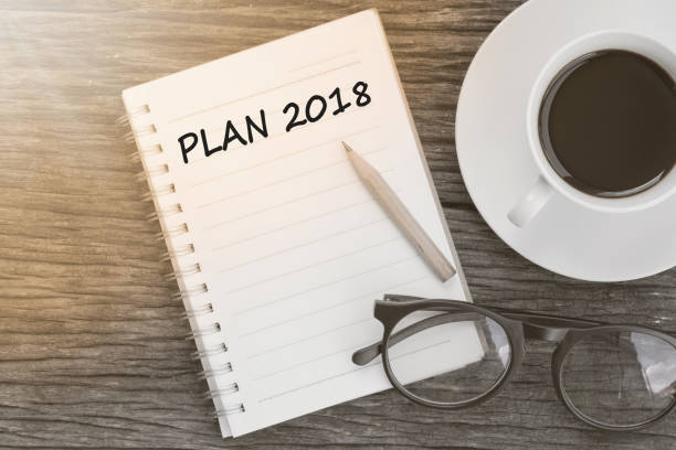 istock Plan 2018 on notebook with coffee cup, glasses and pencil on wooden background 814084676