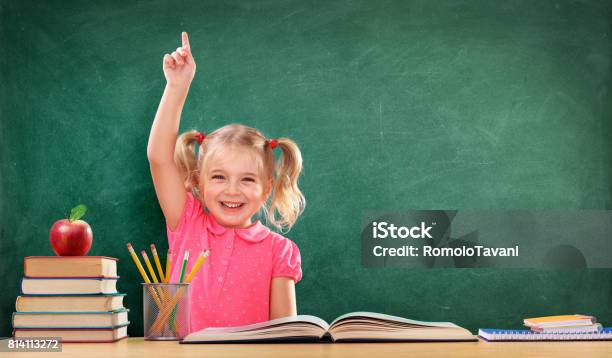 Happy Girl Raising Hand In The Classroom Stock Photo - Download Image Now - Child, Back to School, Hand Raised