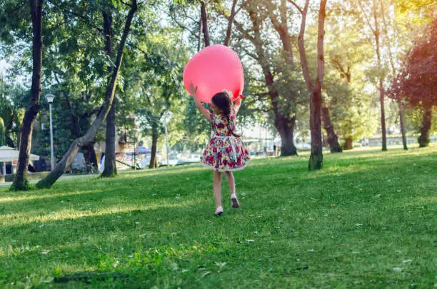 Photo of back view of beauty girl in nature hugging big balloon, awsome girl having fun outside, girl running on green grass copy space