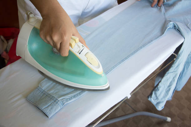 istock woman ironing shirt on ironing board with steaming iron 814189380