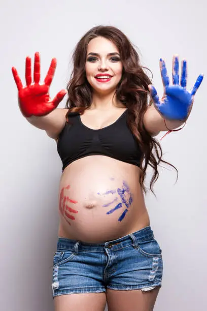 Smiling pregnant woman with bodyart. Prints of the red and blue palm on the abdomen. Determining the future gender of the child
