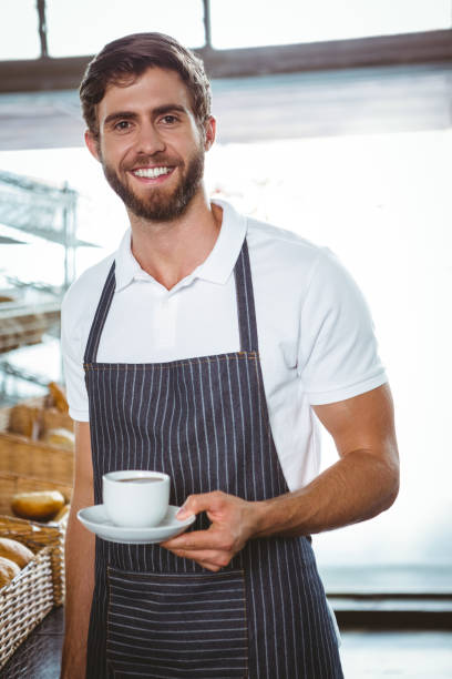 istock happy worker in apron holding a cup of coffee 814252478