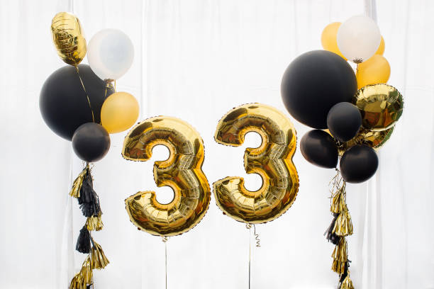 Decoration for 33 years birthday, anniversary Decoration for birthday, anniversary, celebration of the thirty-third anniversary, white background, gold and black balloons with tassels number 33 stock pictures, royalty-free photos & images