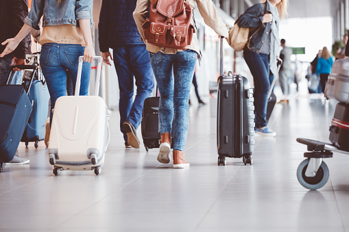 Low angle rear view of passengers walking in the airport terminal. People with luggage in airport.