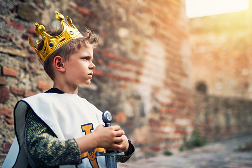 Young king at the castle walls. The boy is holding a sword and is deep in thought. The future of his kingdom is depending on his decisions.
