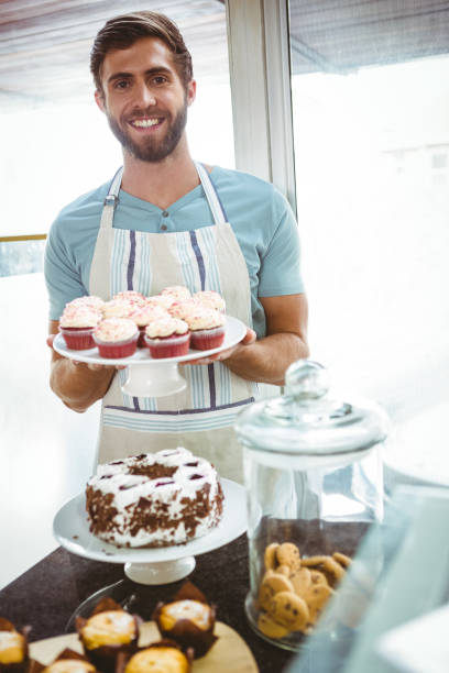 istock Smiling worker holding cupcakes behind the counter 814282184
