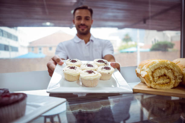 istock Smiling worker holding cupcakes behind the counter 814285754