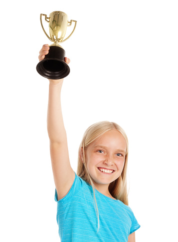 A little blonde pre-teen smiles happily as she holds the silver trophy she's just won up over her head.