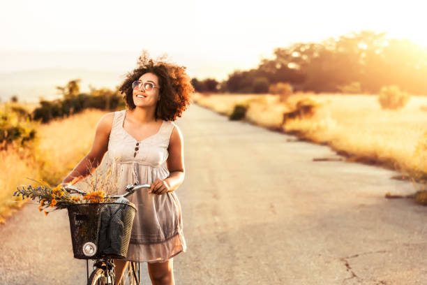 Smiling african woman enjoying nature view, with bicycle, at sunset.