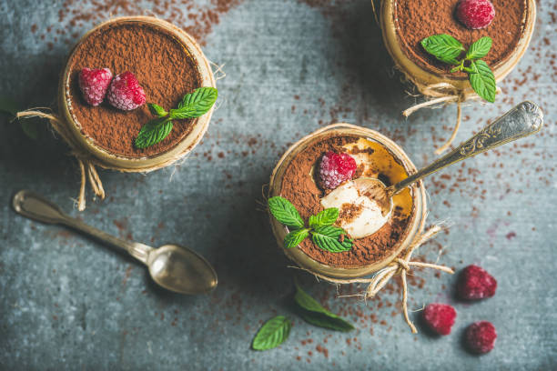 Homemade dessert Tiramisu in glasses with berries and mint Homemade Italian dessert Tiramisu served in individual glasses with fresh mint leaves, raspberries and cocoa powder over grey concrete background, top view, selective focus tiramisu glass stock pictures, royalty-free photos & images