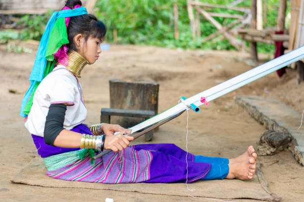 Long Neck Village in Thailand CHIANG MAI, THAILAND - July 10, 2017: Karen hill-tribe (Long Neck) woman weaving fabrics for a living at her house in a tribe near Chiang Mai in Northern Thailand. kayan neck rings stock pictures, royalty-free photos & images