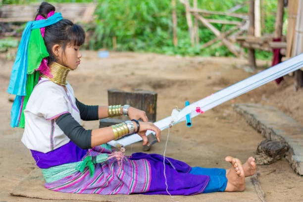 Long Neck Village in Thailand CHIANG MAI, THAILAND - July 10, 2017: Karen hill-tribe (Long Neck) woman weaving fabrics for a living at her house in a tribe near Chiang Mai in Northern Thailand. kayan neck rings stock pictures, royalty-free photos & images