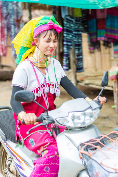 Long Neck Village in Thailand CHIANG MAI, THAILAND - July 10, 2017: Long Neck woman riding a bike in a tribe near Chiang Mai in Northern Thailand. kayan neck rings stock pictures, royalty-free photos & images