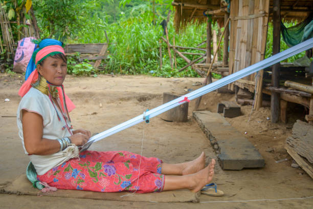 Long Neck Village in Thailand CHIANG MAI, THAILAND - July 10, 2017: Karen hill-tribe (Long Neck) woman weaving fabrics for a living at her house in a tribe near Chiang Mai in Northern Thailand. kayan neck rings stock pictures, royalty-free photos & images